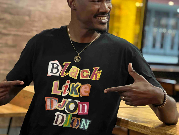Marc Robert creole Sizzle founder wearing a black t-shirt with colorful text Black Like Djondjon , sitting at a table in a casual setting.